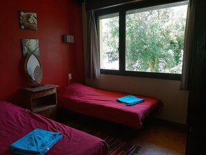 Ein Zimmer mit zwei Betten, einem Spiegel und einem Fenster mit Blick auf Bäume.