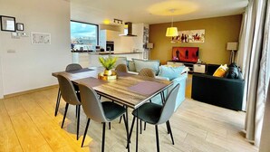 Ein modernes Wohnzimmer mit Essbereich, einem Fernseher und einer Küche im Hintergrund.