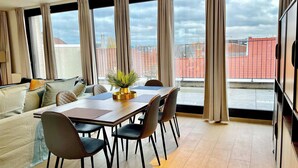 Ein Essbereich mit Tisch, Stühlen und Blick auf Gebäude durch große Fenster.
