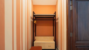 Un pasillo estrecho con una litera, un banco de madera y una puerta.