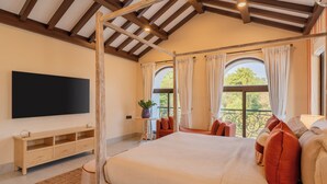 Un dormitorio con una cama grande, televisión, balcón con cortinas y techo de madera.