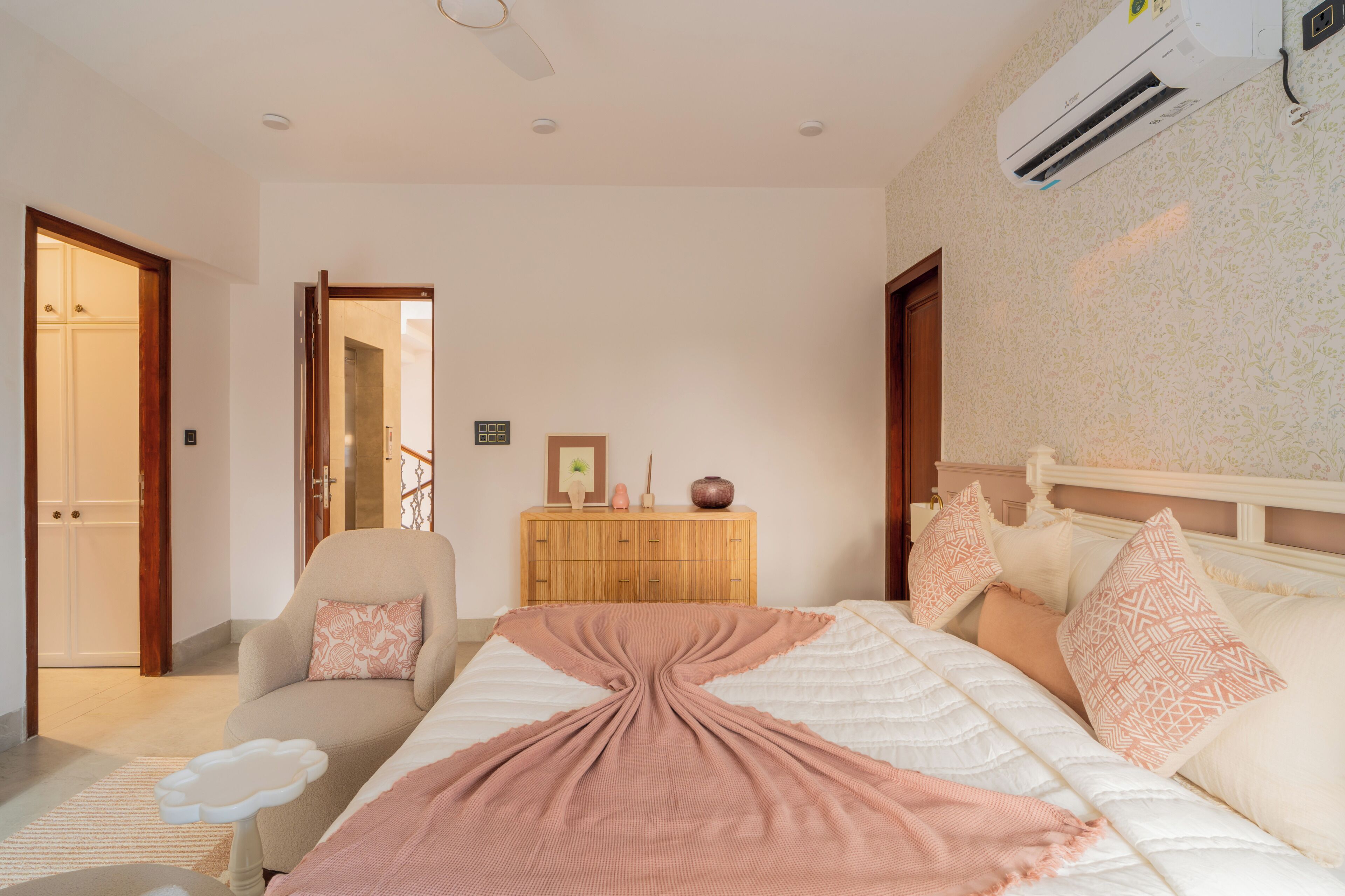 A bedroom with a bed, a chair, a dresser, and an air conditioning unit.