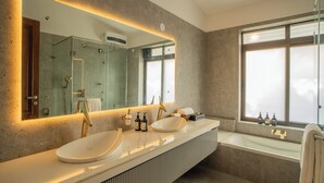 Un baño moderno con un espejo grande, dos lavamanos, una bañera y una ventana con vistas.