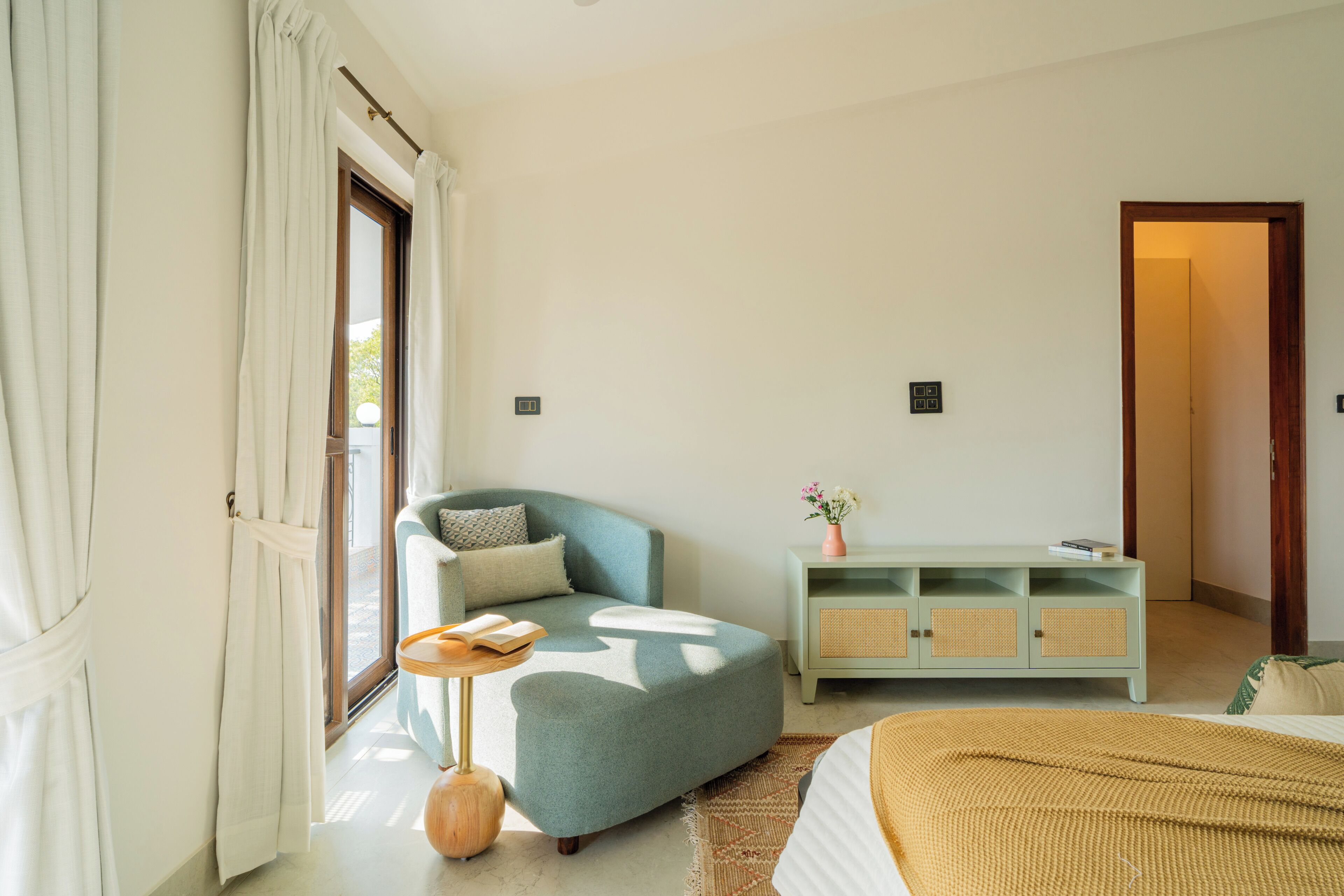 A bedroom with a bed, a sofa, a small table, a cabinet, and a door leading to another room.