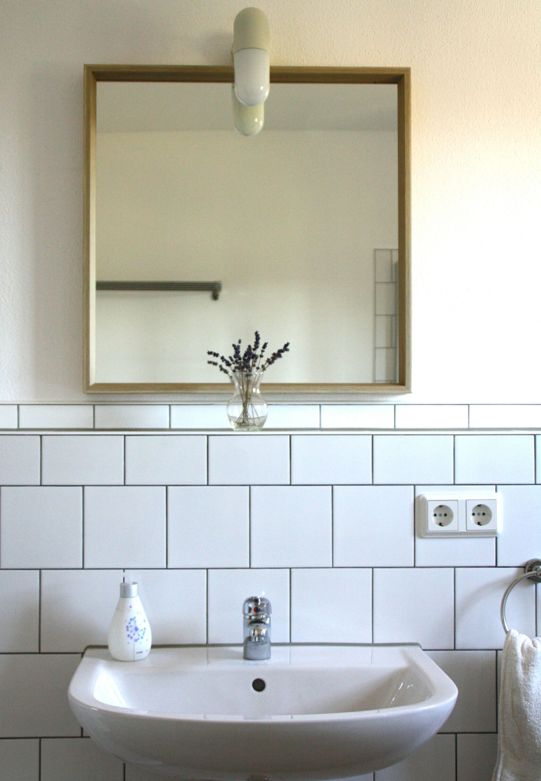 Une salle de bain avec un lavabo blanc, un miroir et un vase de fleurs.