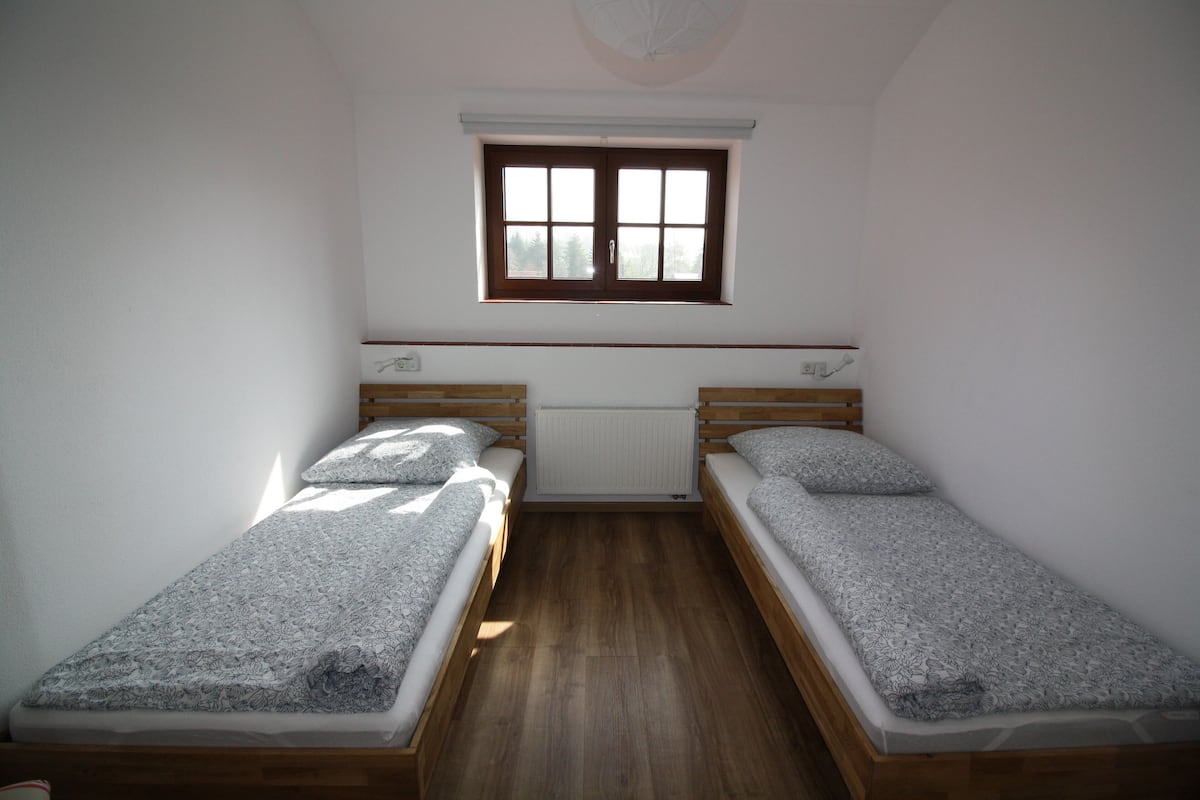 Een kleine kamer met twee eenpersoonsbedden, een raam en een radiator.