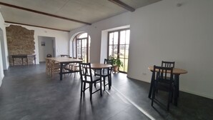 A spacious room with a large dining table, several chairs, a stone wall, and large windows. - Ferienhof Steindörfel (Hochkirch)