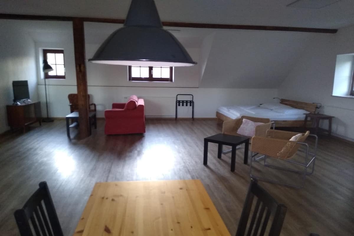 Een kamer met een houten eettafel, een rode bank, een bed en een grote zwarte lamp.