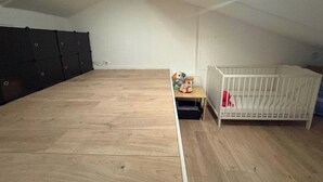 Een kamer met een houten vloer, een wit wiegje en een klein tafeltje met speelgoed.
