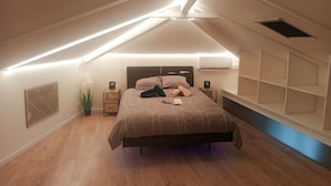 Een slaapkamer met een schuine kap, een bed, nachtkastjes, een wandairconditioner en een potplant.