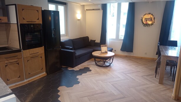 Een moderne keuken met een zwarte koelkast, houten kastjes en een eethoek met een tafel en stoelen.