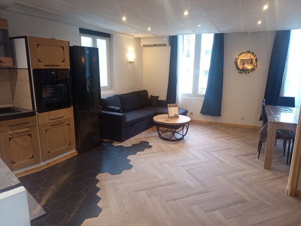 A modern kitchen with a black refrigerator, wooden cabinets, and a dining area with a table and chairs. - Duplex Nice Pessicart (Nice)