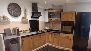 Een moderne keuken met houten kastjes, een zwarte koelkast, een gasfornuis en een koffiezetapparaat.