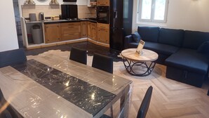 Een moderne keuken met houten kastjes, een zwarte koelkast en een eethoek met een tafel afgedekt met plastic.
