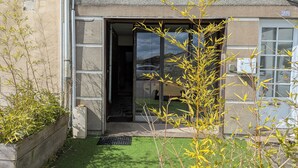 En bygningseingang med en glasdør, et lille haveområde med kunstgræs og en træplantekasse.
