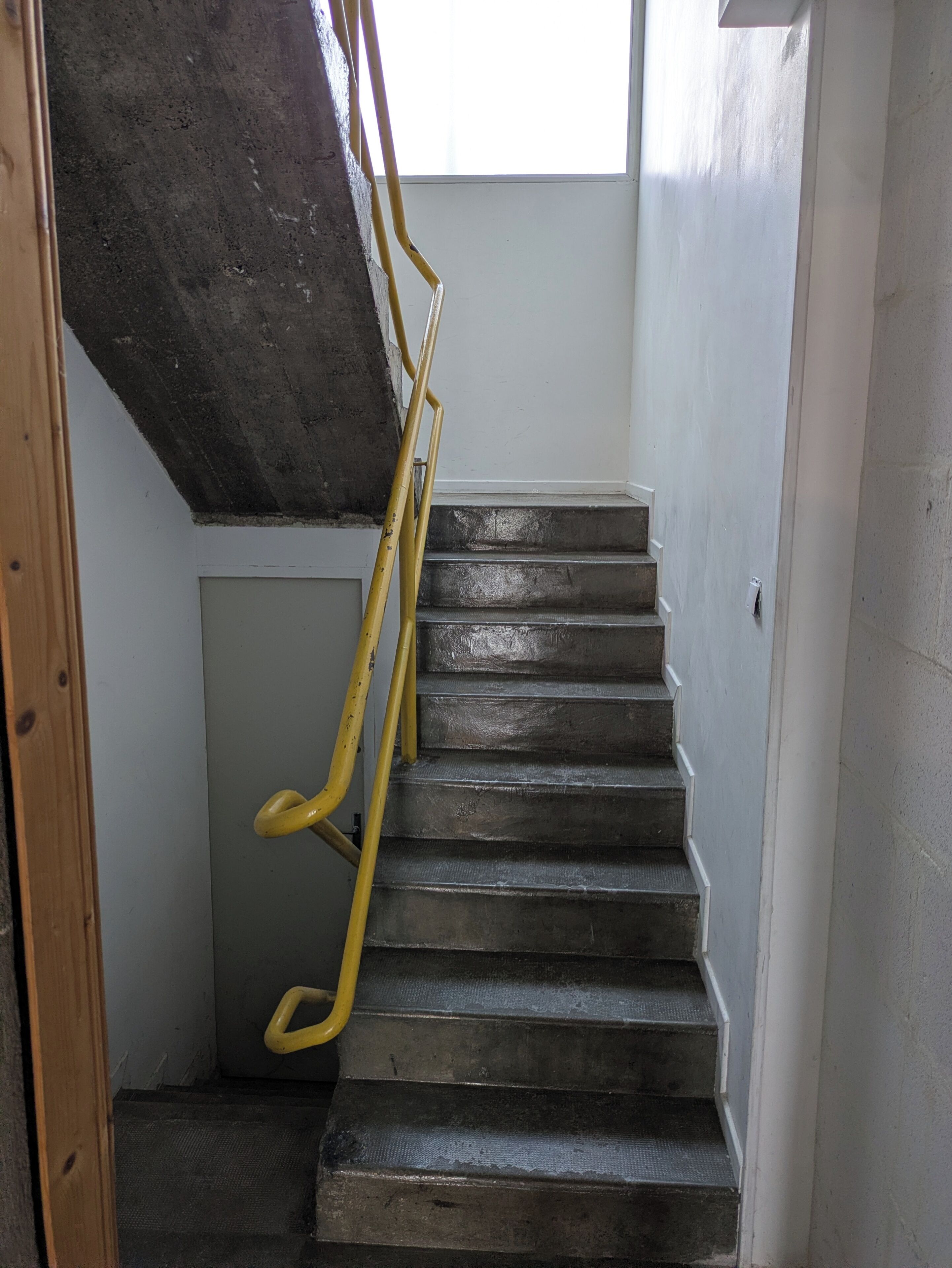 Een trap met een houten leuning en een betonnen muur.