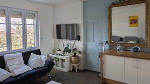 En stue med en sort sofa, fjernsyn, en dør og et spejl.
