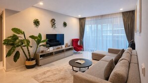 Una sala de estar moderna con un sofá, una silla roja, un televisor y ventanas amplias.