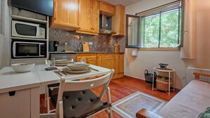 A compact kitchen with wooden cabinets, a microwave, a toaster oven, and a dining area with a chair and table. - Your comfortable shelter with pool - Herbasabina 2 (Pla de l'Ermita)