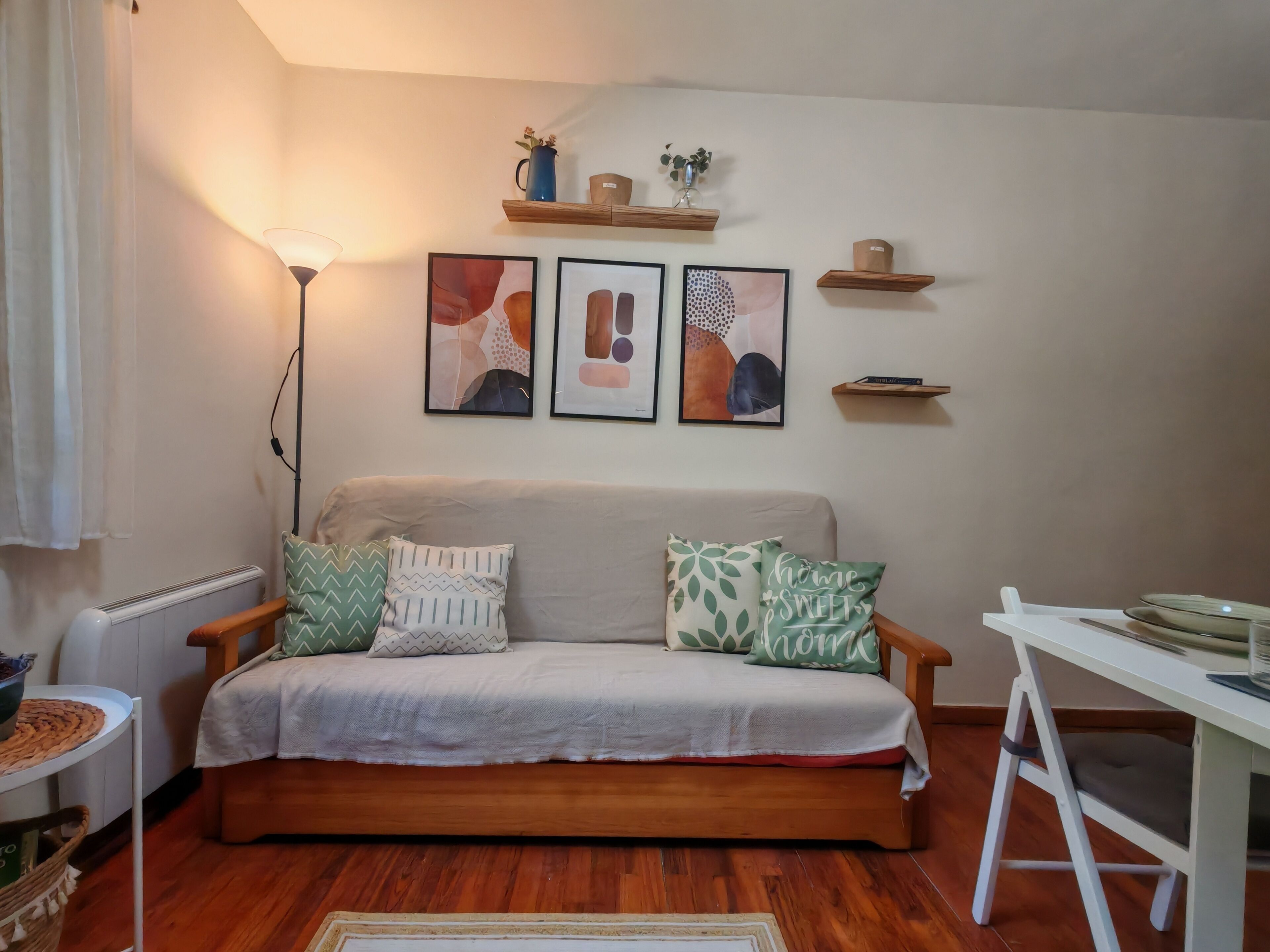 Ein gemütliches Wohnzimmer mit einer Couch, einer Stehlampe und an Wänden befestigten Regalen mit dekorativen Gegenständen.