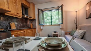 A compact kitchen with wooden cabinets, a granite countertop, a dining table set with plates, glasses, and cutlery, and a window with a view of greenery. - Your comfortable shelter with pool - Herbasabina 2 (Pla de l'Ermita)