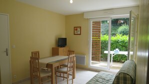 Una habitación con una mesa de comedor, sillas, un televisor sobre un mueble, un sofá y una puerta corrediza de vidrio que da a un jardín.