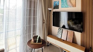Una sala de estar moderna con ventilador de techo, un televisor montado en un panel de madera y una ventana con cortinas traslúcidas.