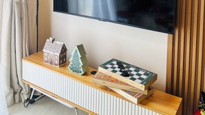 Un televisor de pantalla plana montado en la pared, una pequeña consola de madera con un árbol de Navidad, un tablero de ajedrez y una maqueta de una casa.
