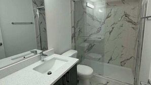 Un baño con ducha de mármol, un espejo grande y un lavamanos moderno.