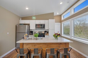 Una cocina moderna con una isla central, electrodomésticos de acero inoxidable y vistas a zonas verdes por la ventana.