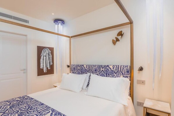 A hotel room with a bed, a bedside table, a wall-mounted towel rack, and a patterned headboard.