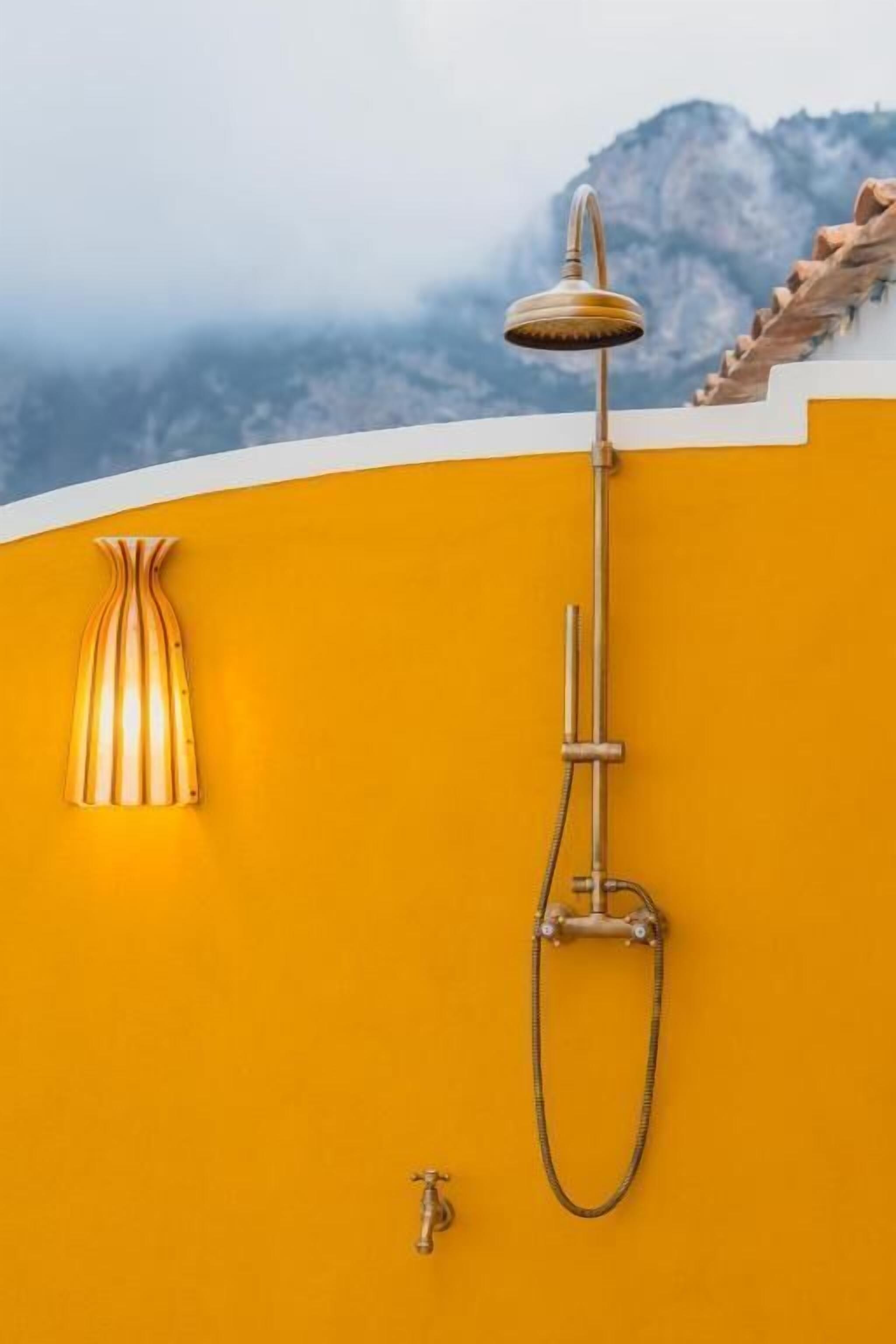 A bathroom with a shower, a faucet, and a wall-mounted light fixture against a yellow wall.