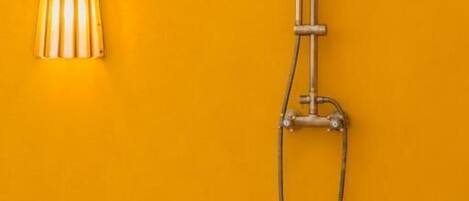 A bathroom with a shower, a faucet, and a wall-mounted light fixture against a yellow wall.