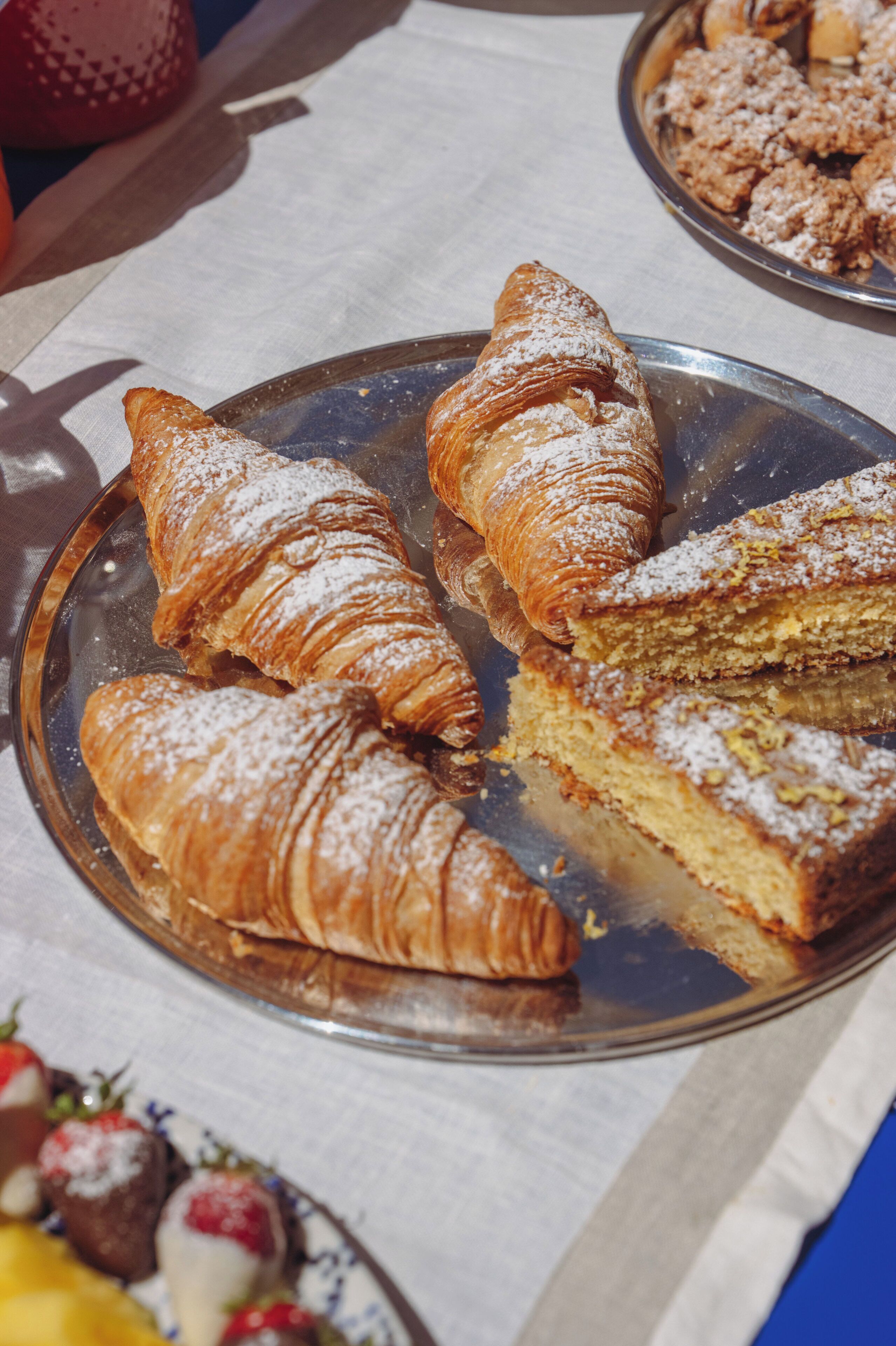 Une assiette en métal contenant des pâtisseries, notamment des croissants et une part de gâteau, posée sur une nappe.
