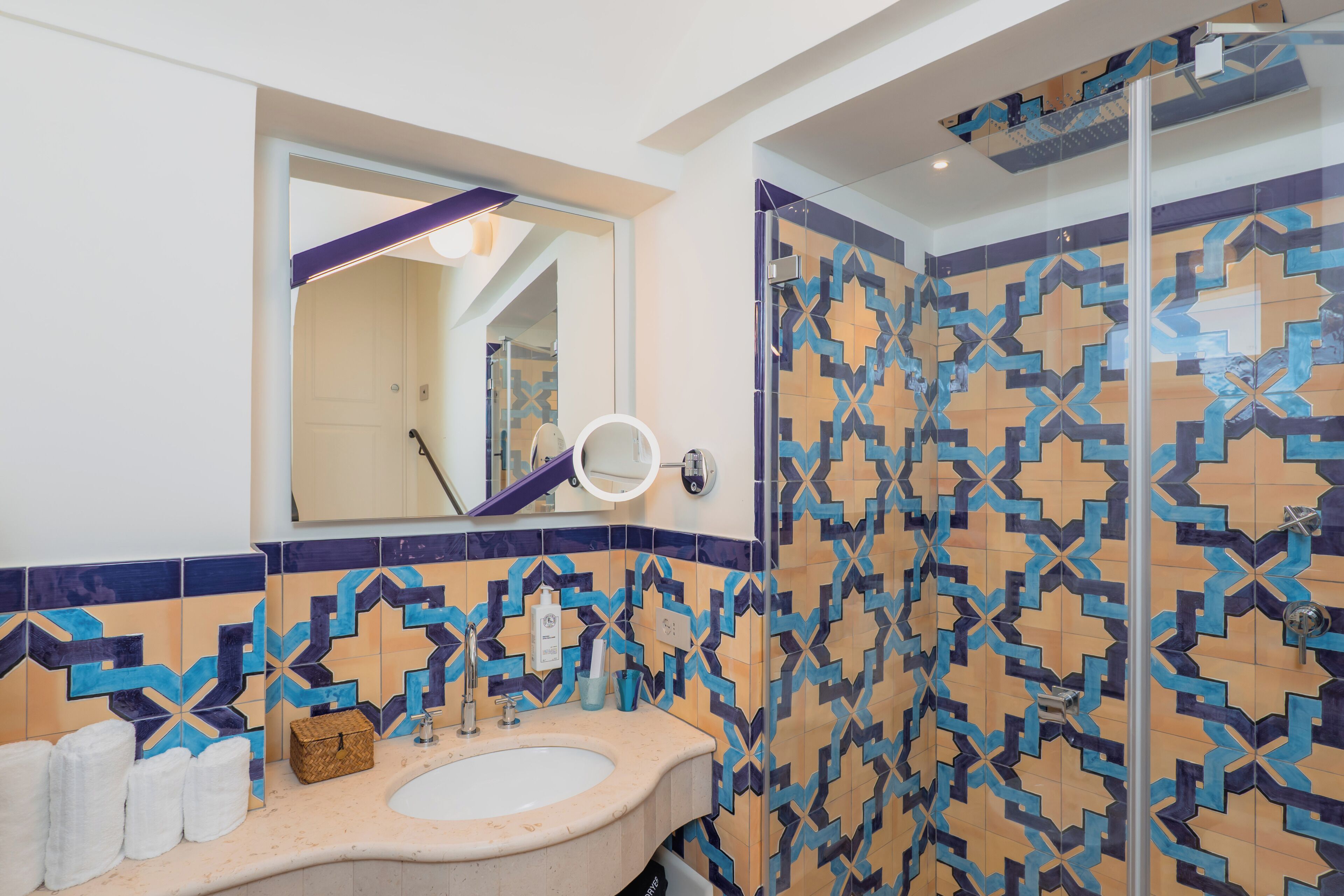 Un baño con lavabo, espejo y azulejos estampados.