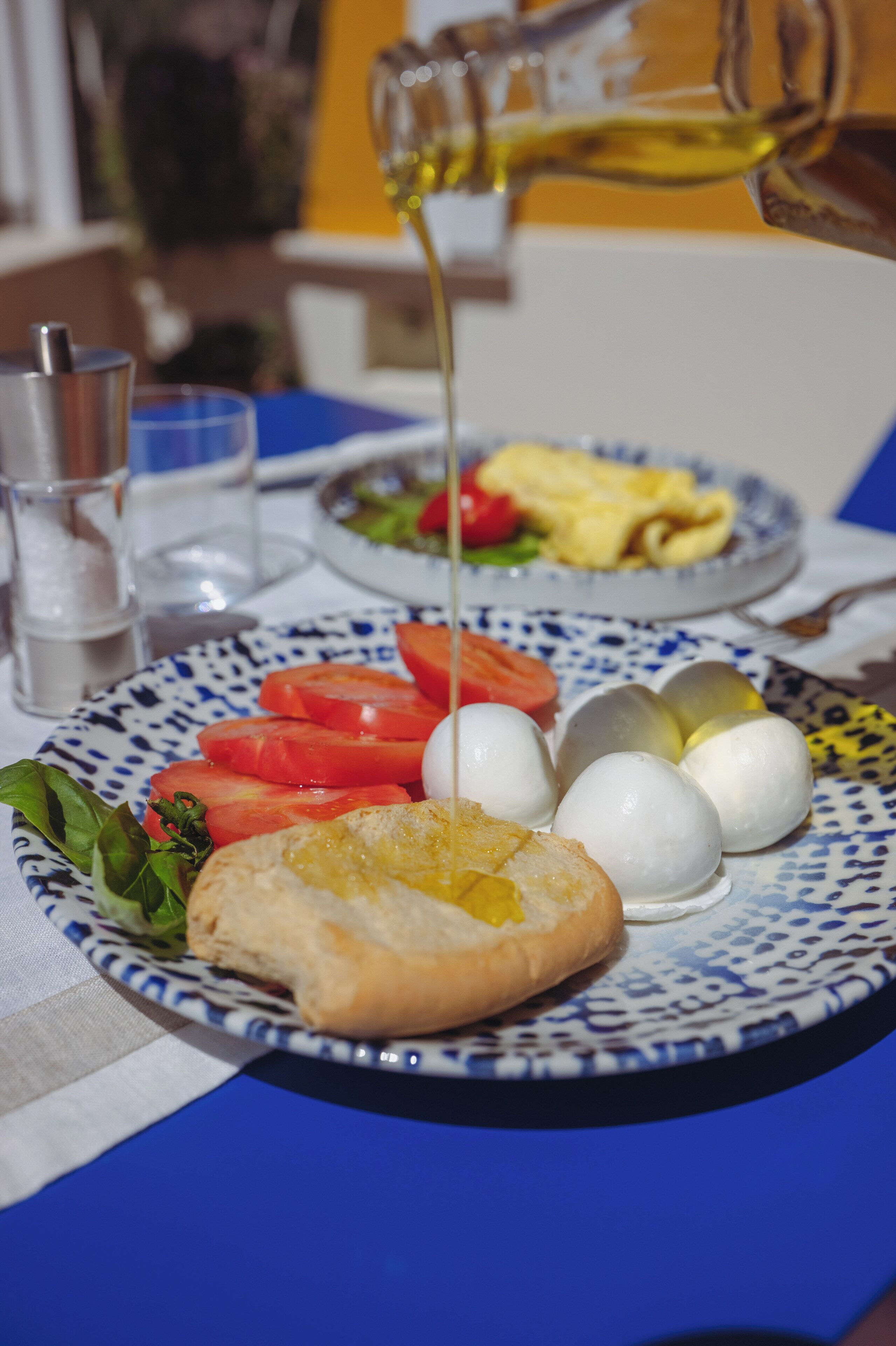 Um prato com tomates fatiados, ovos e um sanduíche, com um copo de água e uma salada ao fundo.
