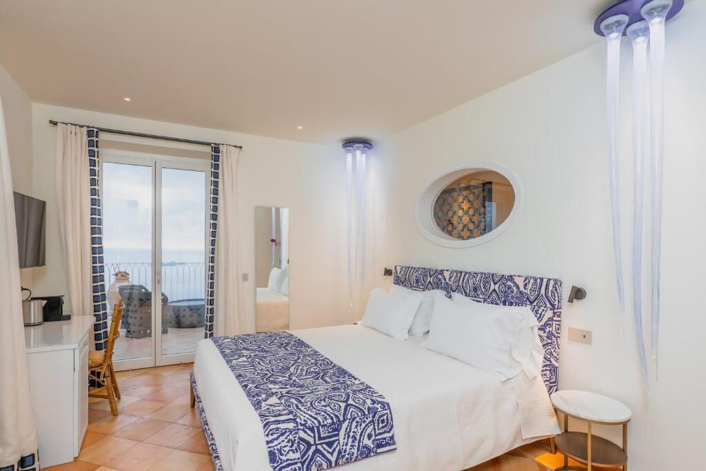 A bedroom with a bed, a round mirror, a TV, and a balcony with a table and chair.
