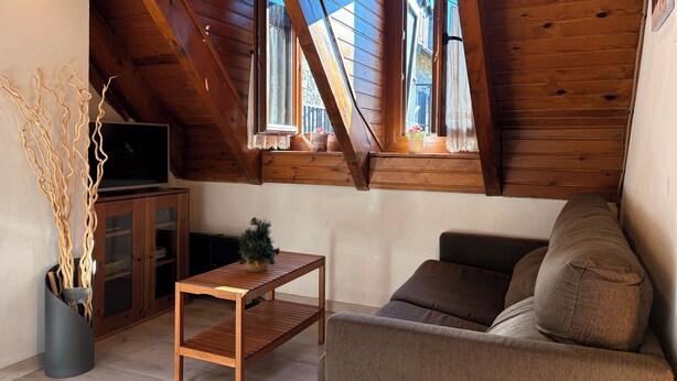 Une chambre à coucher confortable, aménagée en mezzanine, avec des poutres en bois, une table en bois, un canapé et un téléviseur.