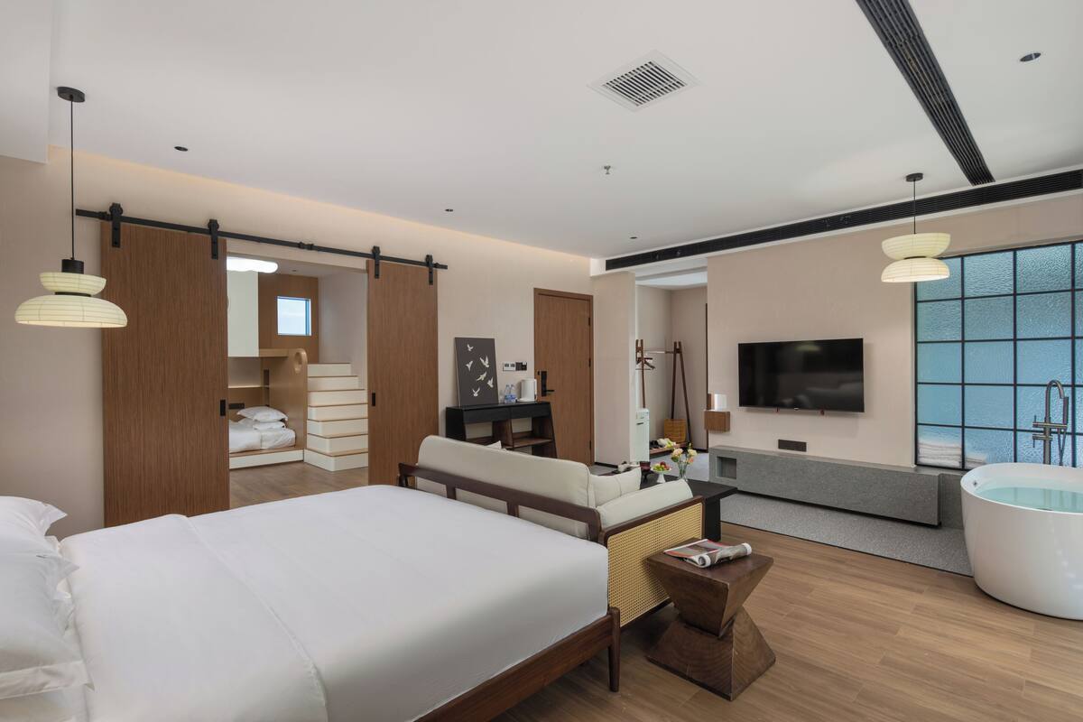 Een moderne hotelkamer met een groot bed, een zithoek, een televisie, een ligbad en een groot raam.