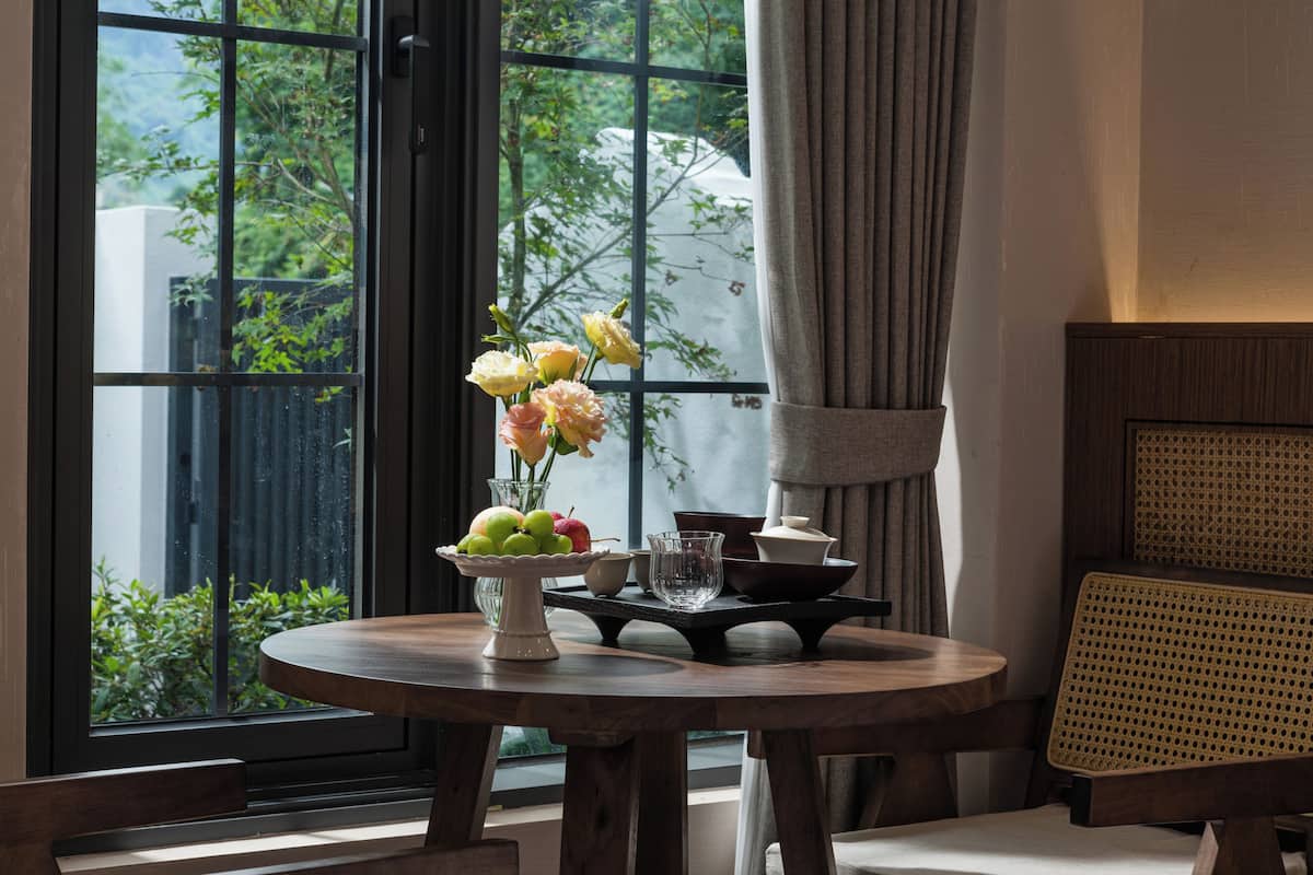Een ronde houten tafel met een fruitschaal, een vaas met bloemen en een glas.