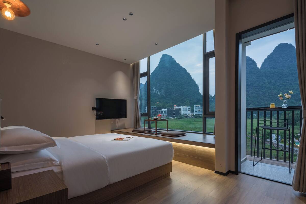Een slaapkamer met een groot bed, een aan de muur bevestigde televisie en een balkon met uitzicht op bergen.