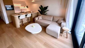 A modern living room with a sofa, a small table, and a kitchen area with a bar. - Luxury Apartment With sea View (Middelkerke)