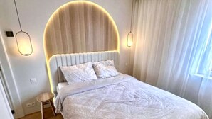 A modern bedroom with a curved headboard, a bed with a patterned bedspread, and two pendant lights. - Luxury Apartment With sea View (Middelkerke)