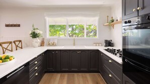 A modern kitchen with dark cabinetry, a white countertop, and a large window. - The Meadow Yarra Valley Spa Sauna (Yarra Glen)