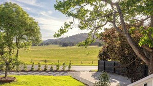 A residential property with a well-maintained lawn, a driveway, and a view of a green field and hills in the distance. - The Meadow Yarra Valley Spa Sauna (Yarra Glen)