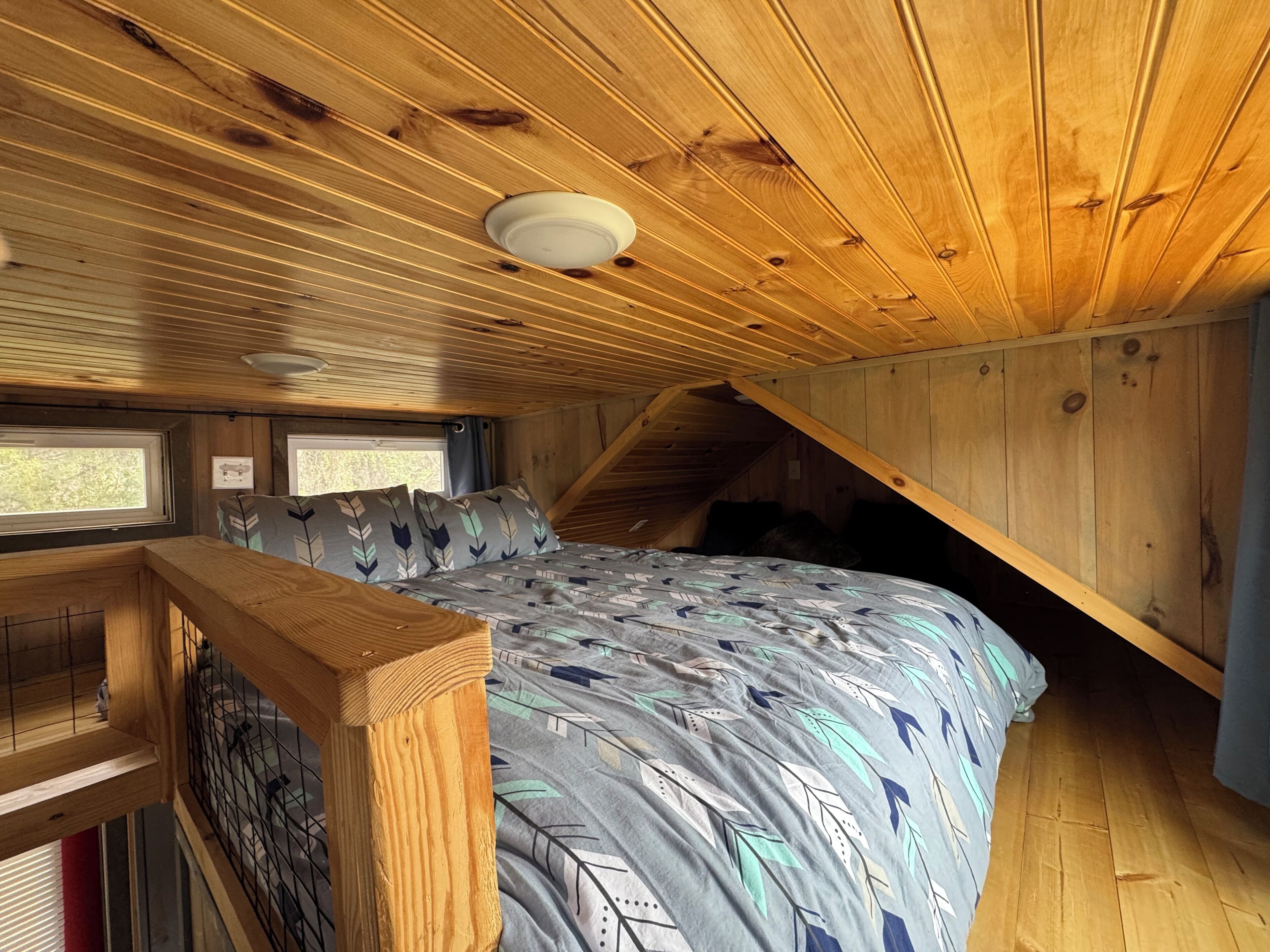 A bedroom with a bed, wooden ceiling, and a window.