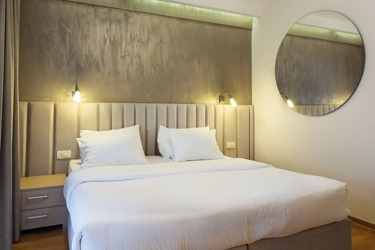 A bedroom with a bed, bedside tables, a round mirror, and wall-mounted lighting.