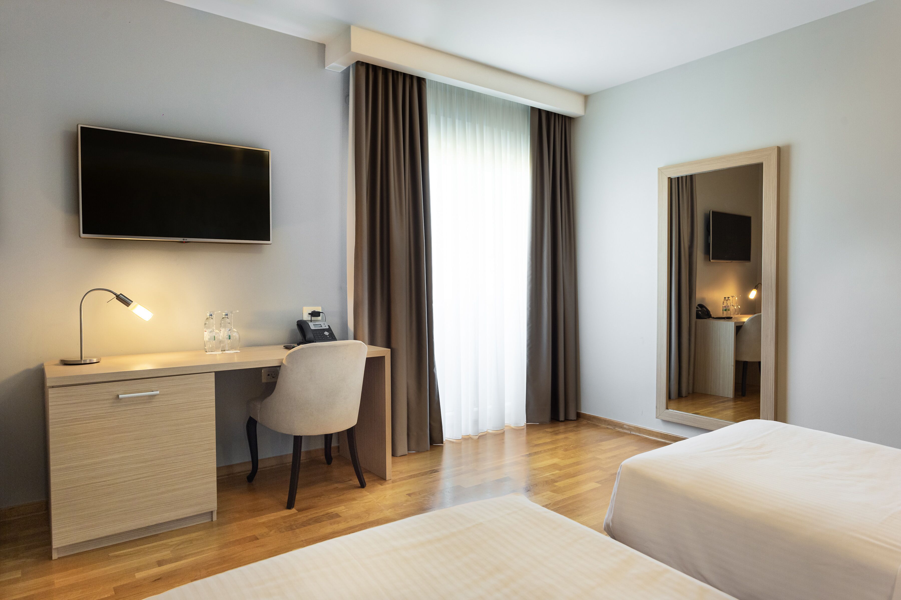 A hotel room with a desk, chair, bed, TV, and a mirror.