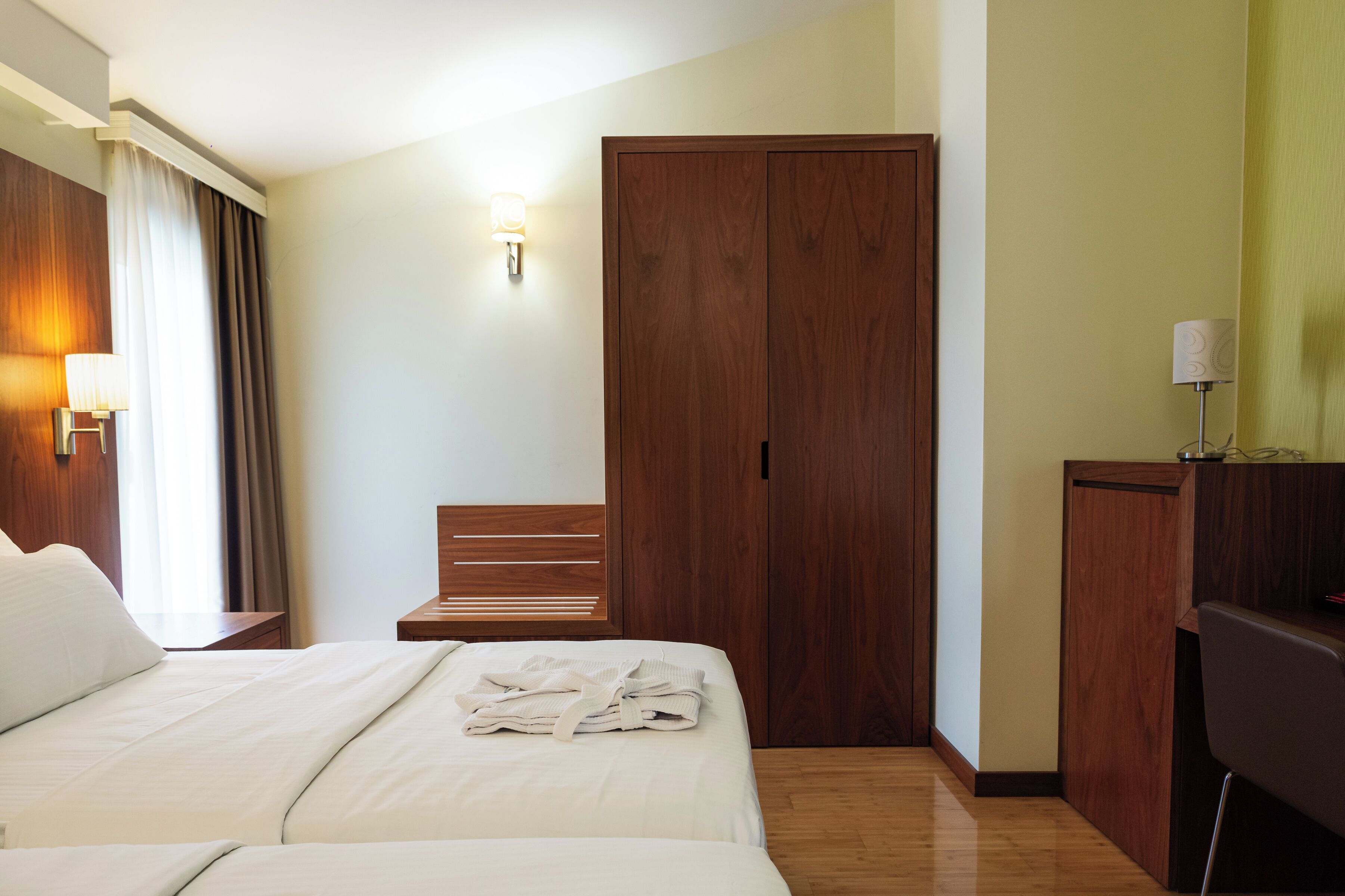Ein Hotelzimmer mit Bett, Holzschrank, Schreibtisch mit Lampe und Stuhl.