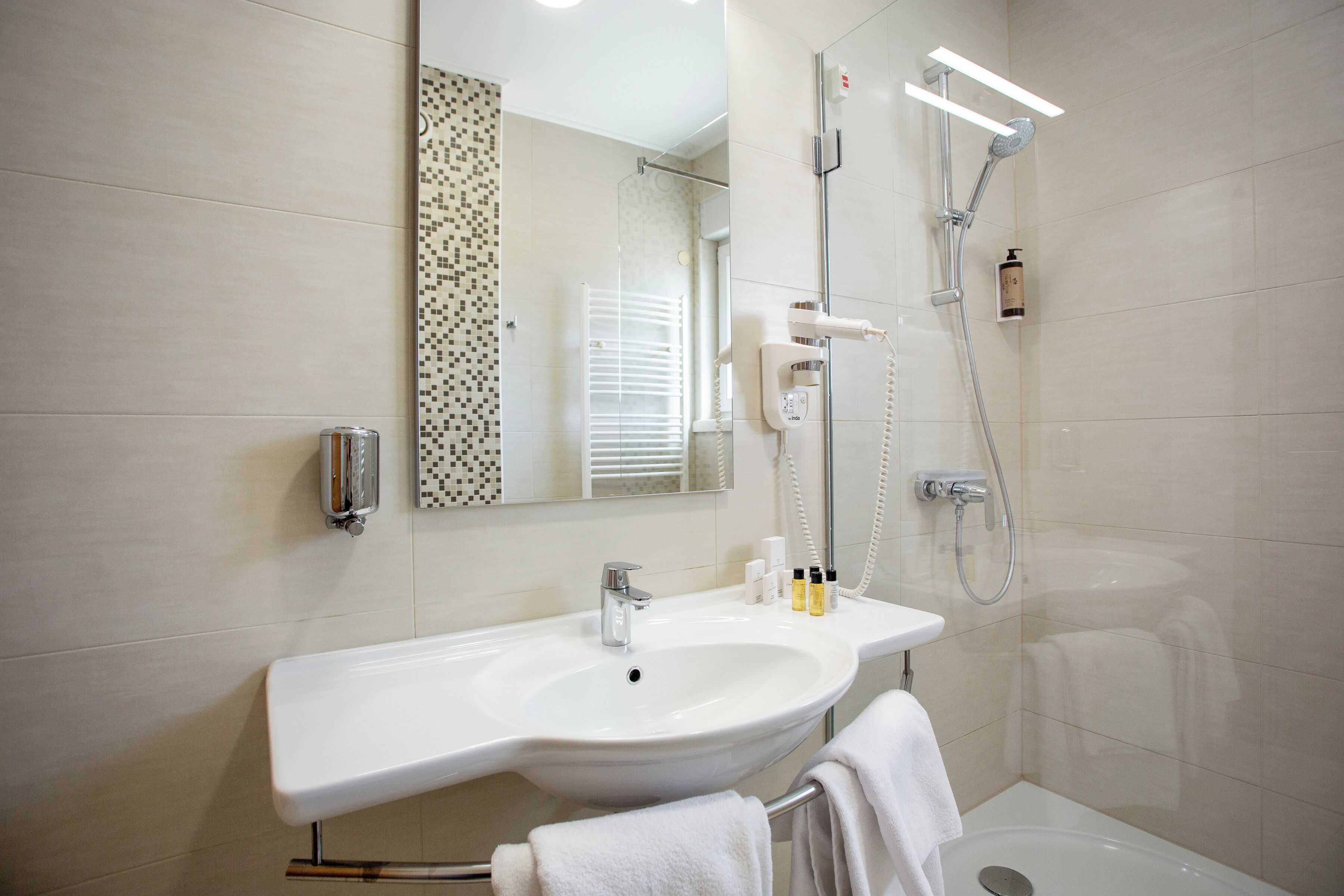 Un bagno moderno con lavandino, specchio e doccia, tutti in bianco.